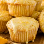 Glazed orange muffins stacked on top of each other on a cutting board.