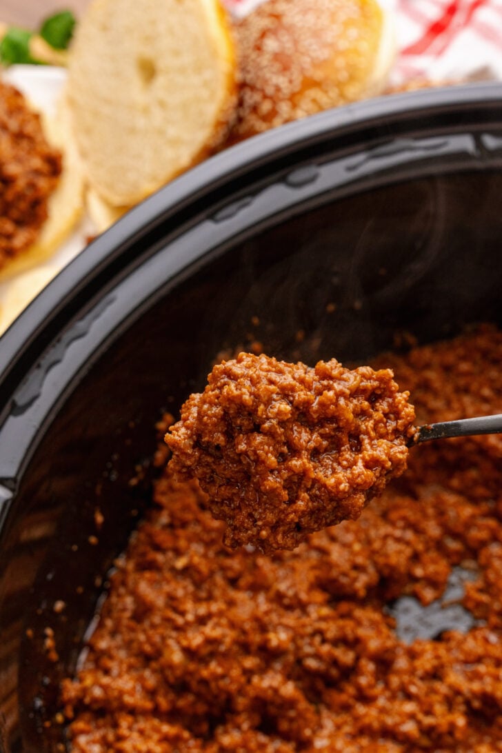 Homemade sloppy joe being spooned out of a black crock pot.