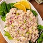 Tunsa salad placed on a green lead of lettuce sitting on a place with fresh lemon slices.