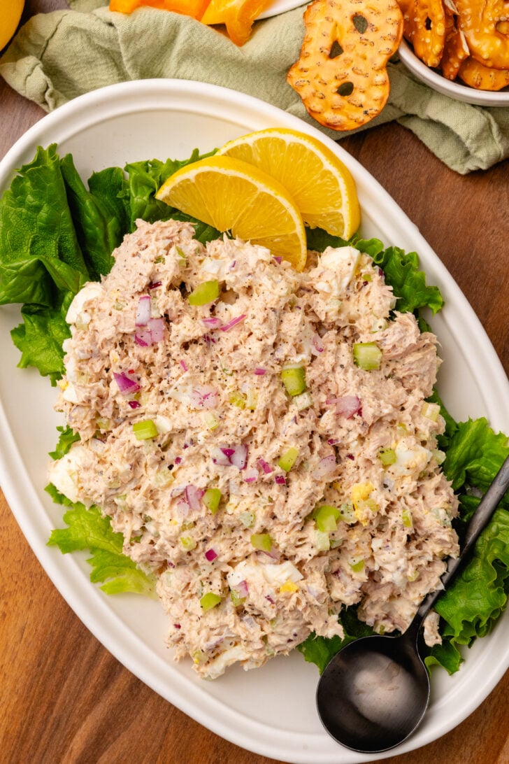 Tuna salad placed on a green lead of lettuce sitting on a place with fresh lemon slices. Make this quick and easy recipe for the All-Time Best Tuna Salad! Flakey tuna is mixed with simple ingredients and a creamy dressing with a bright hint of lemon. It will soon become your go-to tuna salad recipe for lunch or a light dinner.