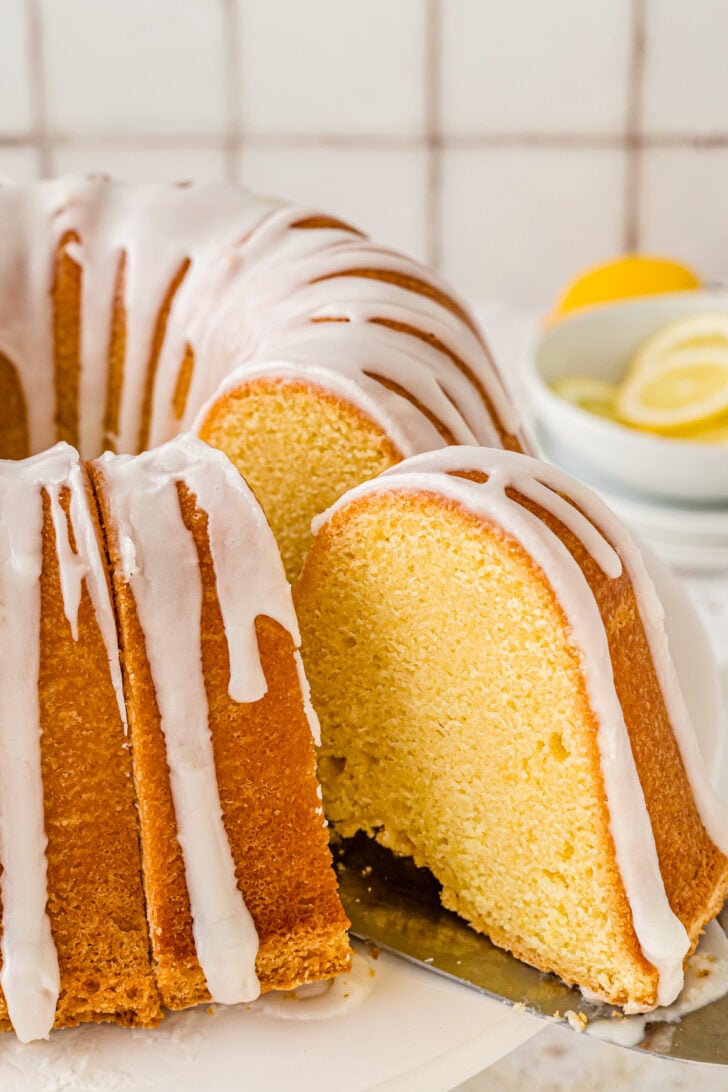 Slice of lemon pound cake with glaze being served from a white cake stand.