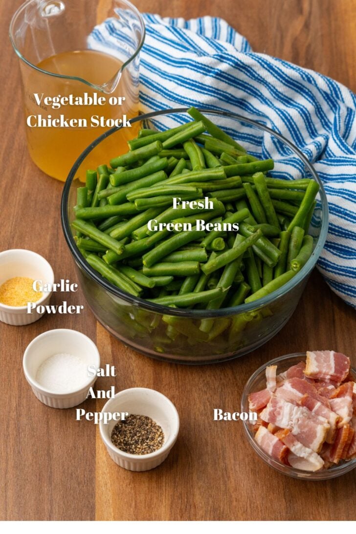 Fresh green beans, vegetable stock, garlic powder, salt, petter and bacon in containers on a wooden board.