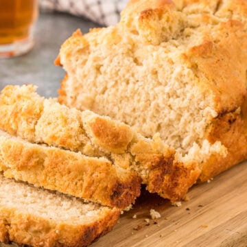 Beer bread sliced perfectly sitting on a wooden cutting board.