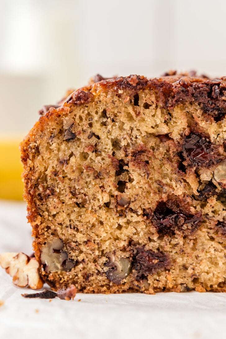 Slice of chocolate chip banana bread with pecans on a piece of parchment paper.
