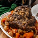 Irish pot roast fresh out of the oven sitting on a bed of carrots and onions on a white serving dish.