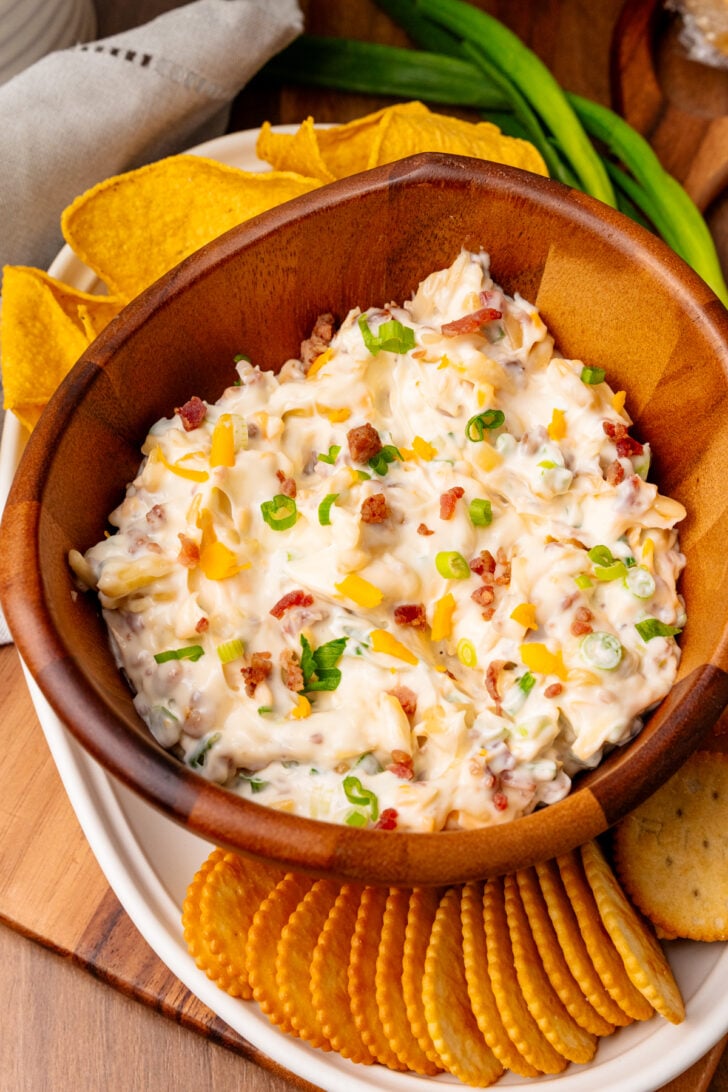 Brown wooden bowl with million dollar dip served with tortilla chips and crackers.