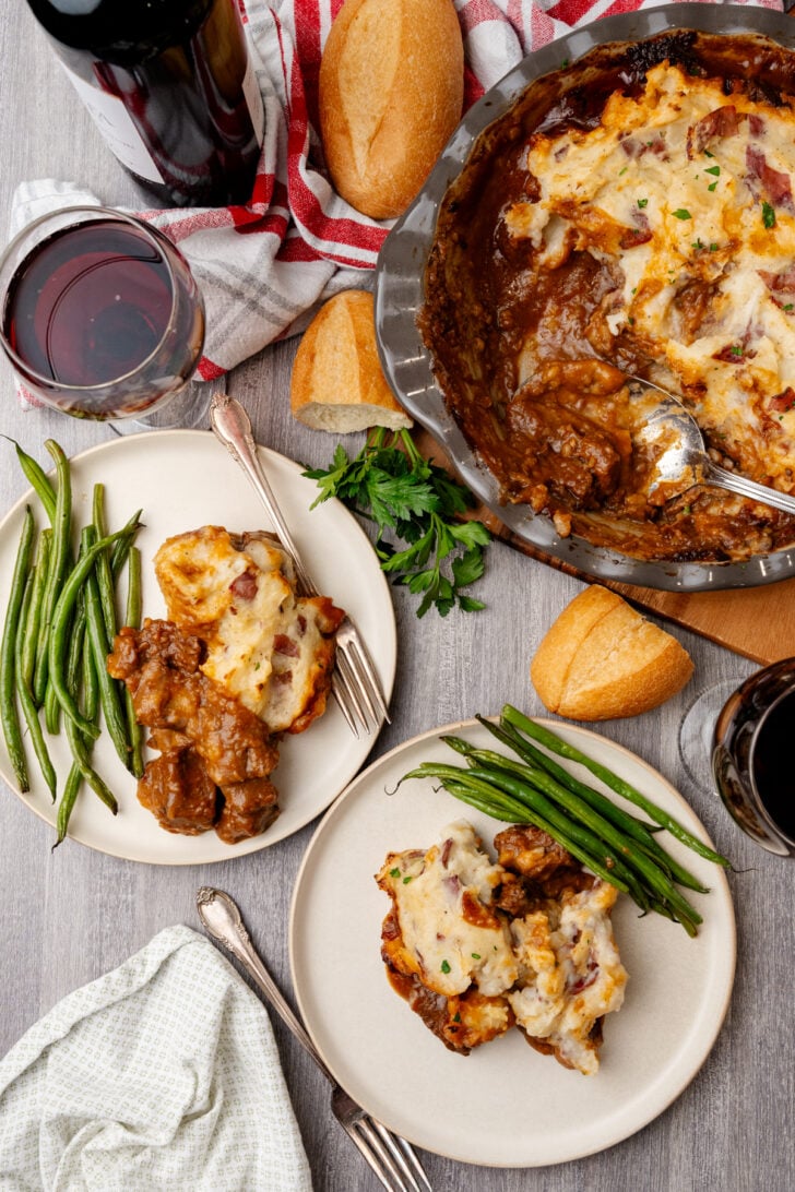 Shepherd's Pie served with green beans, on white plates with a glass of red wine.