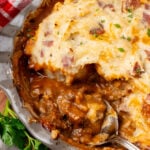 Beef tip pie with mashed potato topping studded with bacon and chives, served in gray bowl on wooden board
