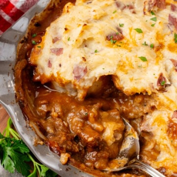 Beef tip pie with mashed potato topping studded with bacon and chives, served in gray bowl on wooden board