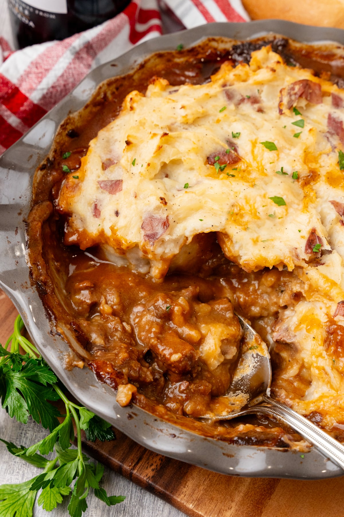 Beef tip pie with mashed potato topping studded with bacon and chives, served in gray bowl on wooden board