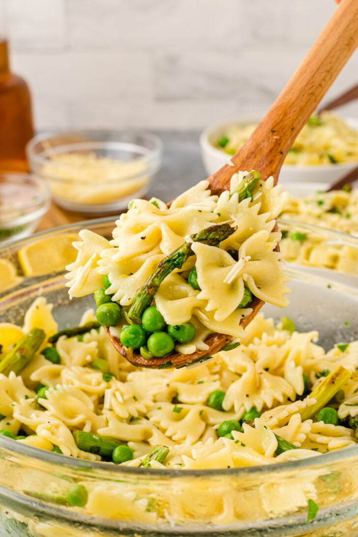 Wooden spoon holding a scoop of bowtie pasta, green peas and asparagus.