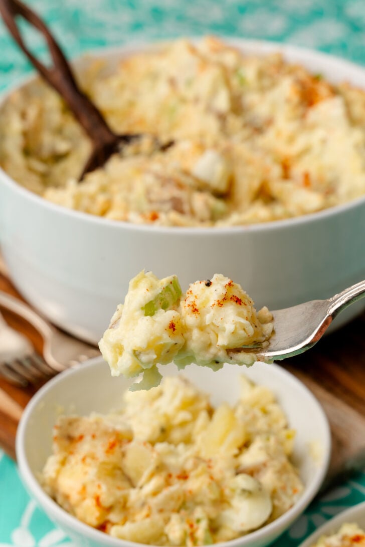 Potato salad scooped up out of a white bowl with a silver fork.