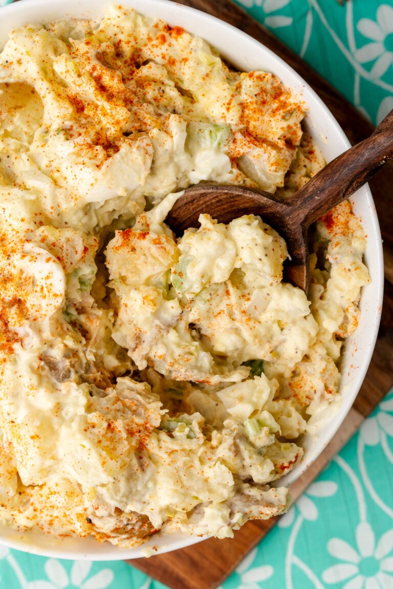 Potato salad scooped out of a bowl with a wooden spoon.