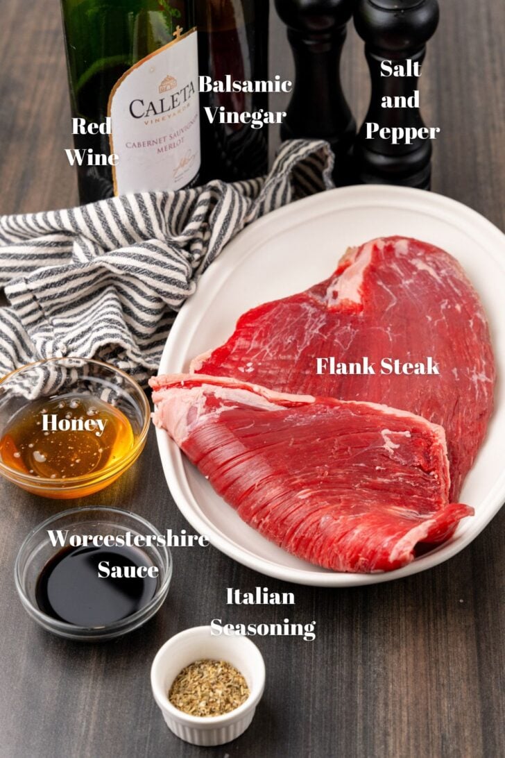 White platter with uncooked flank steak along with italian seaoning, worcestershire sauce, honey, red wine, balsamic vinegar and salt and pepper.