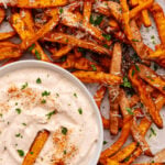 Crispy baked sweet potatoes 12 fries with sea salt and herbs served with creamy dipping sauce on parchment paper