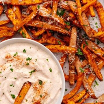 Crispy baked sweet potatoes 12 fries with sea salt and herbs served with creamy dipping sauce on parchment paper