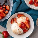 Overhead view of balsamic strawberries with vanilla ice cream in white bowls on teal linen, gray wood surface