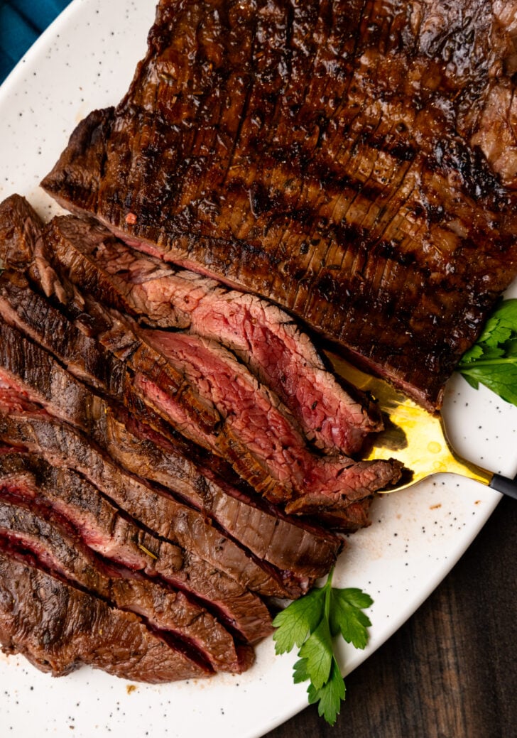 Grilled flank steak, sliced into strips and served on a white plate with a gold fork.