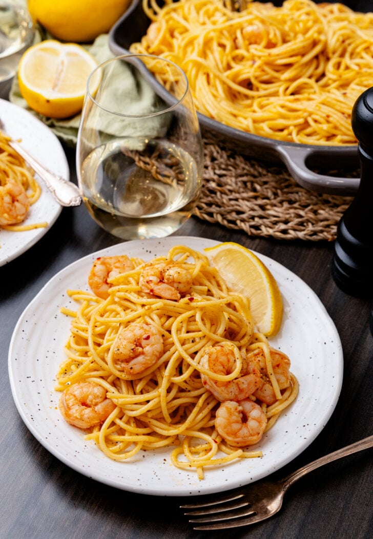 Whitle dinner plate with shrimp scampi and lemon slices with a glass of white wine.