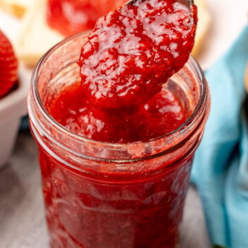 Easy strawberry jam in a glass jar served with a silvere spoon.