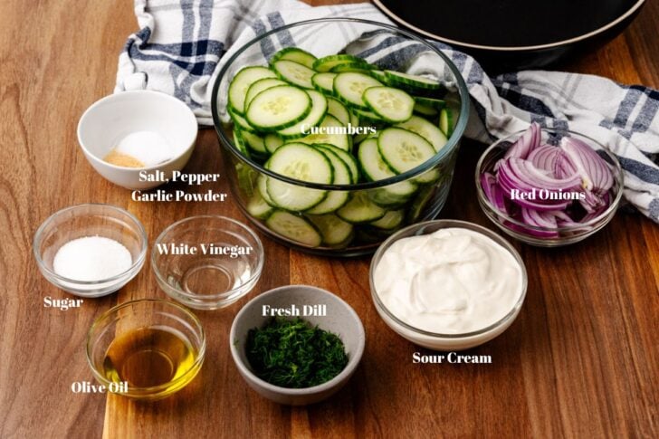 Ingredients for creamy cucumbers salad in glass bowls on a wooden counter.