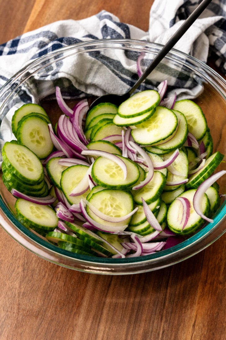 Clear glass bowl with sliced cucumbers and red onions.