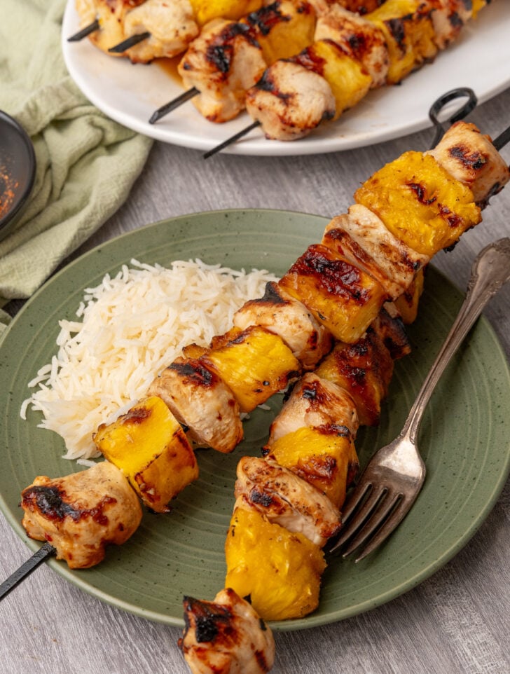 Chicken skewers with a side of rice on a green plate.