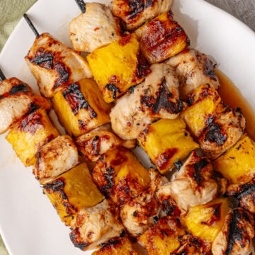 Hawaiian skewers featured on white plate with grilled chicken and pineapple chunks on metal skewers, charred edges visible