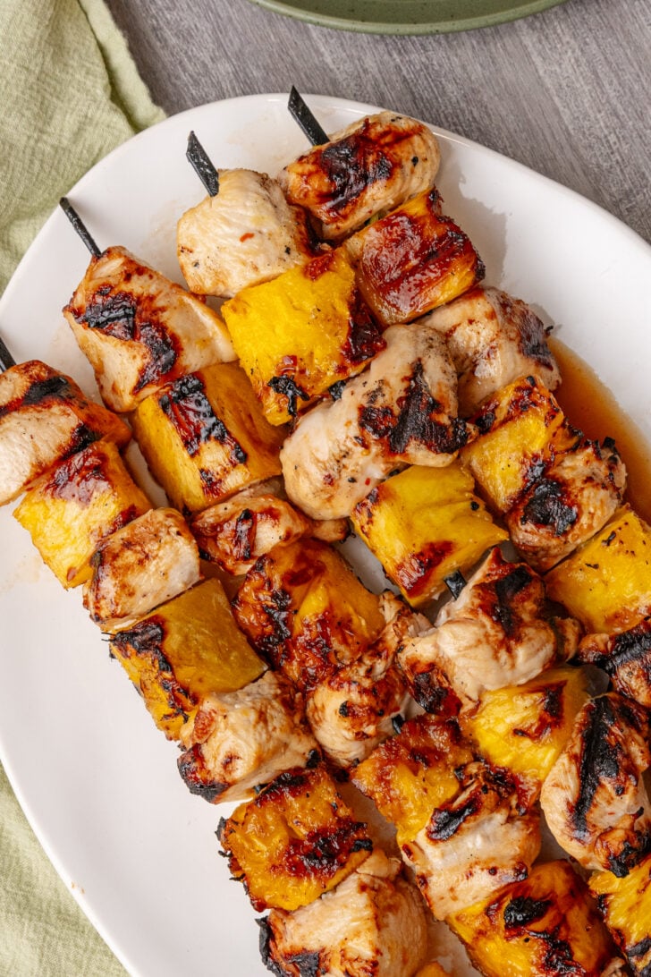 Hawaiian skewers featured on white plate with grilled chicken and pineapple chunks on metal skewers, charred edges visible