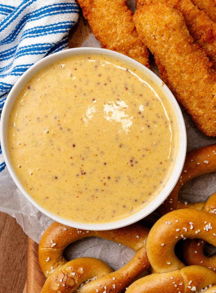 Honey must in a white bowl served with chicken nuggets and pretzels.