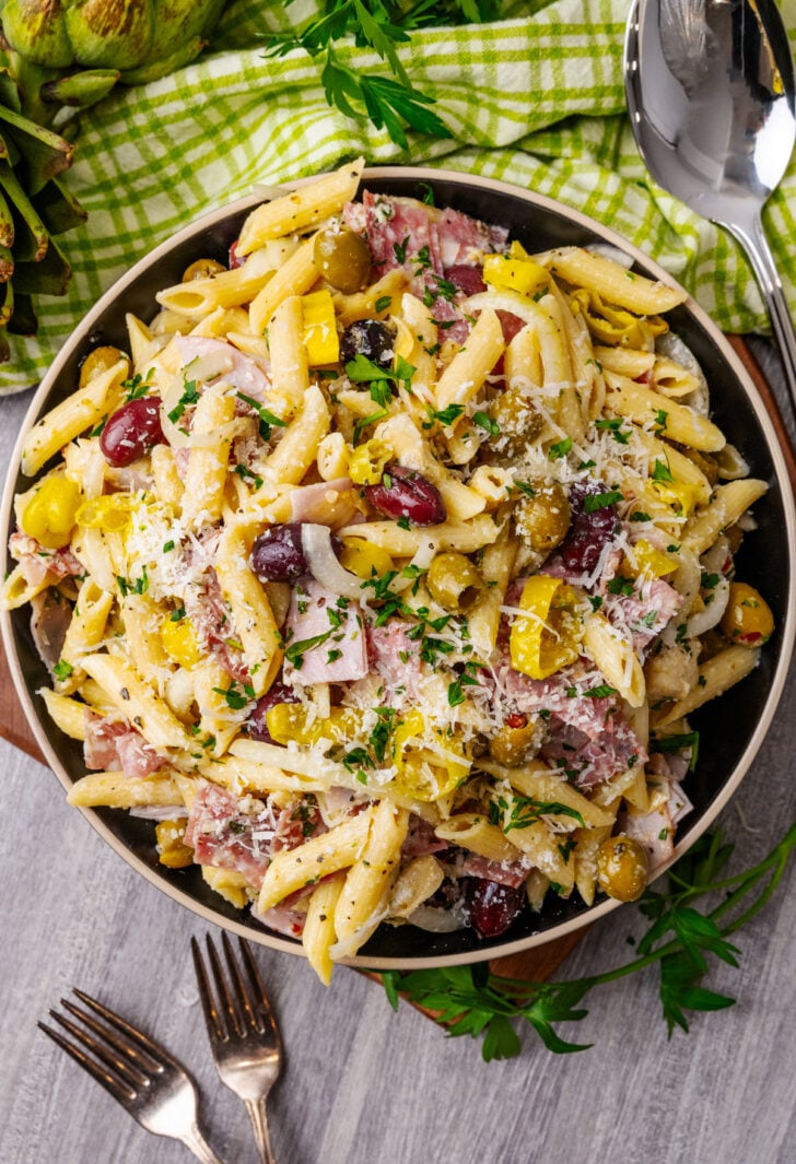 Italian pasta salad 2 3 in black bowl with ham, peppers, olives, cheese, fresh parsley garnish, served with fork