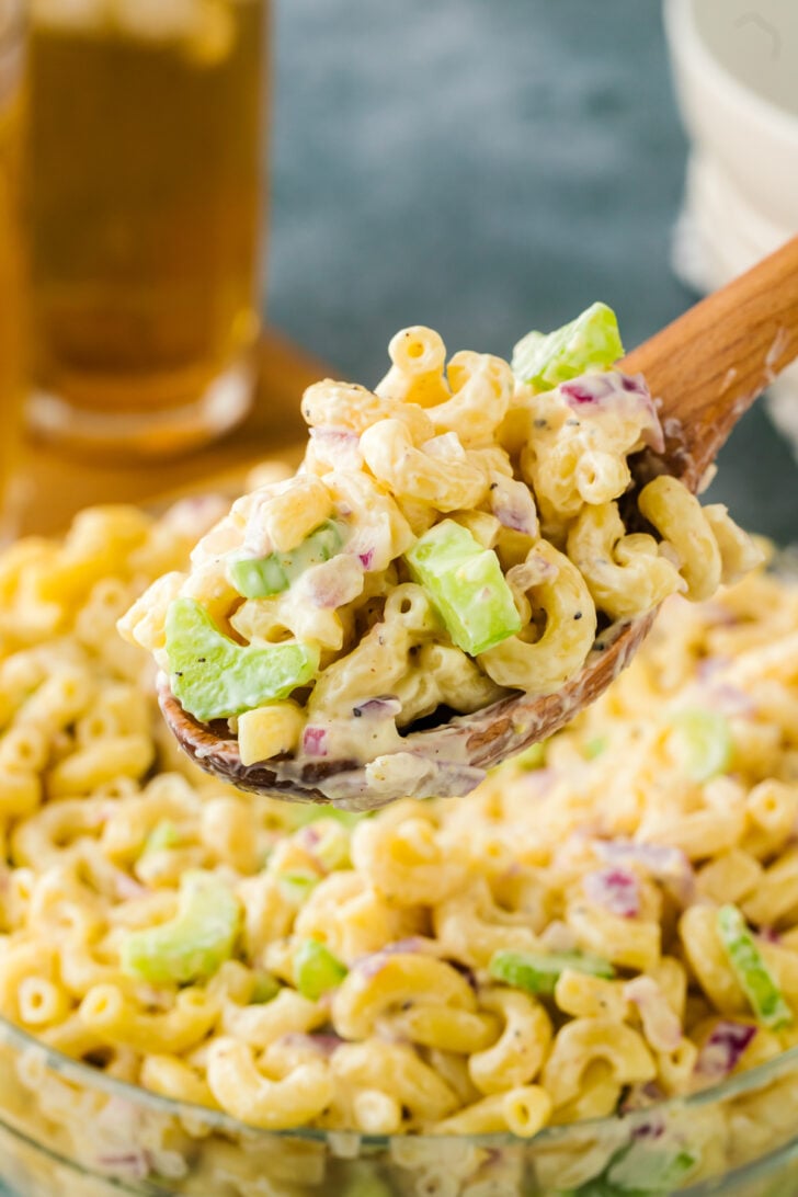 Wooden spoon scooping out macaroni salad with pieces of celery poking out.