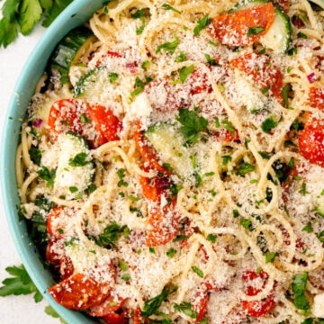 Spaghetti salad 4 in light blue bowl with tomatoes, zucchini, parmesan cheese, fresh parsley, overhead view