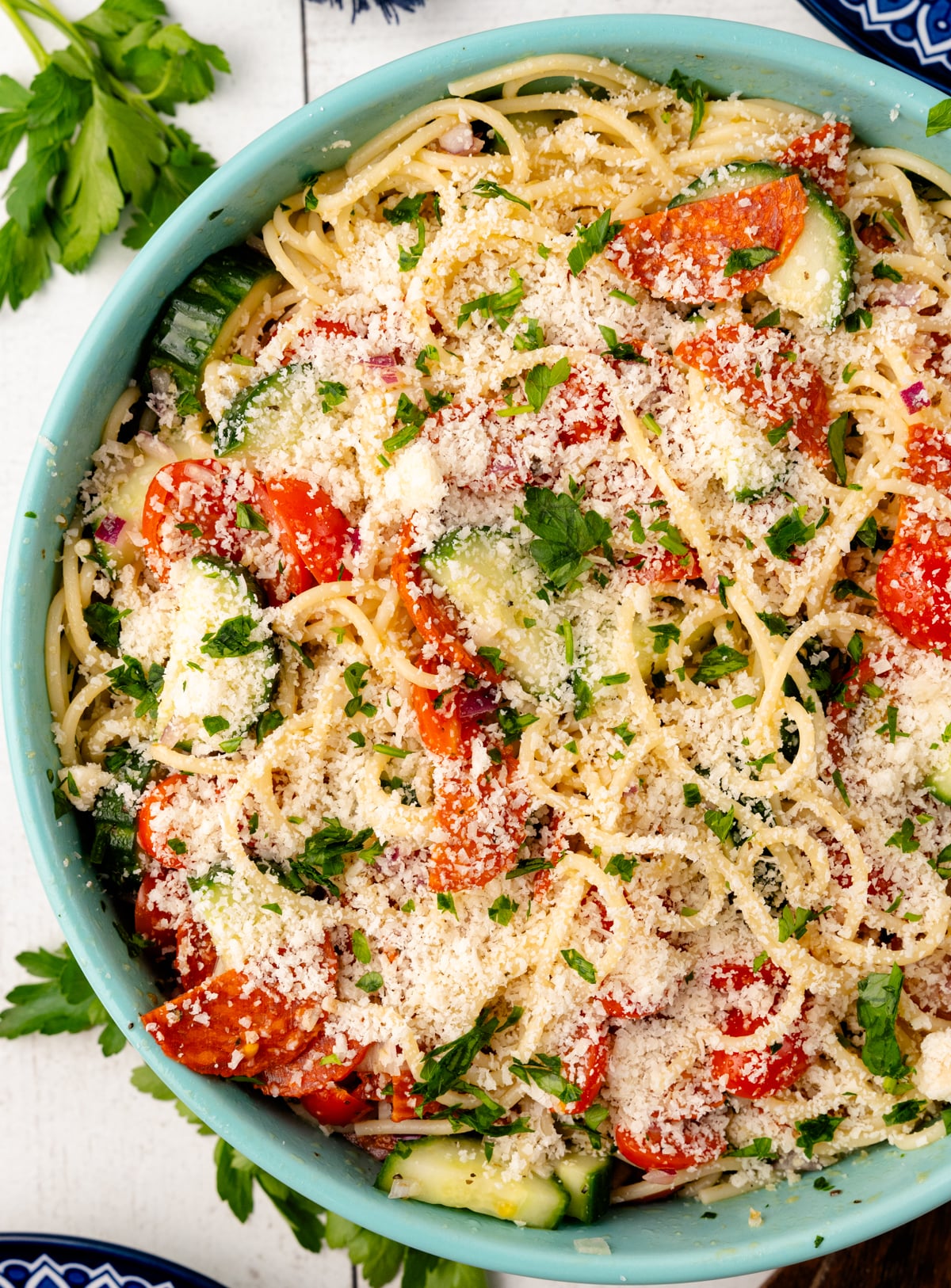 Spaghetti salad 4 in light blue bowl with tomatoes, zucchini, parmesan cheese, fresh parsley, overhead view