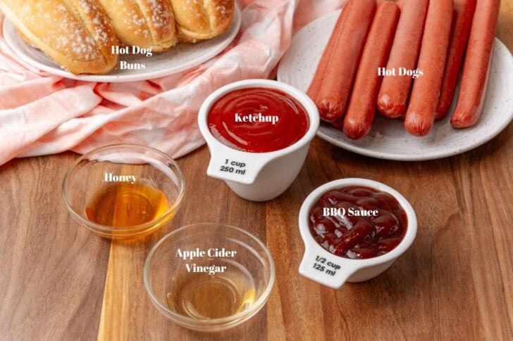 Ingredients for bbq sauce in glass bowls along with hot dogs and hot dog buns.
