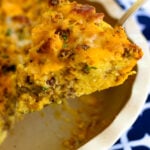 A slice of Sausage Cheese Cornbread Quiche on a spoon over a white bowl, garnished with fresh herbs and black pepper