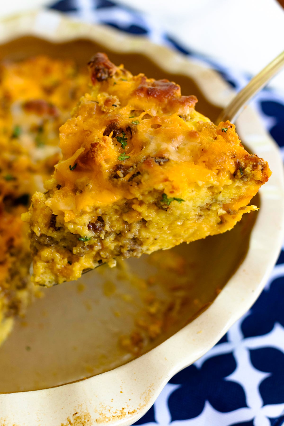 A slice of Sausage Cheese Cornbread Quiche on a spoon over a white bowl, garnished with fresh herbs and black pepper