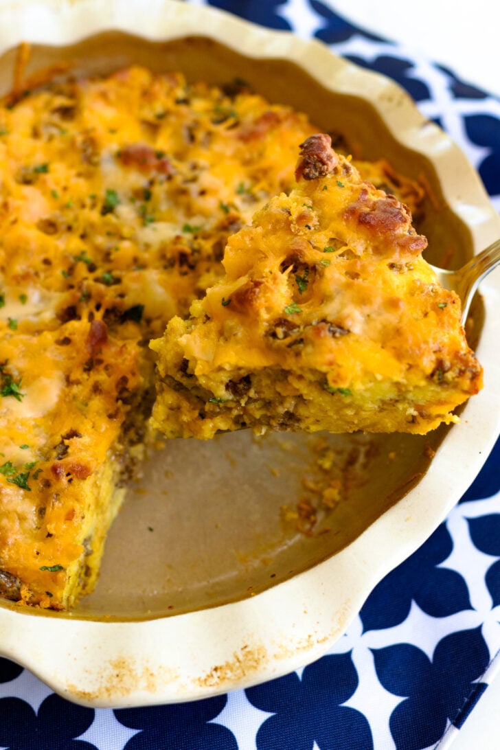 Sausage Cheese Cornbread Quiche baked in white dish with herbs and black pepper garnish on blue patterned tablecloth
