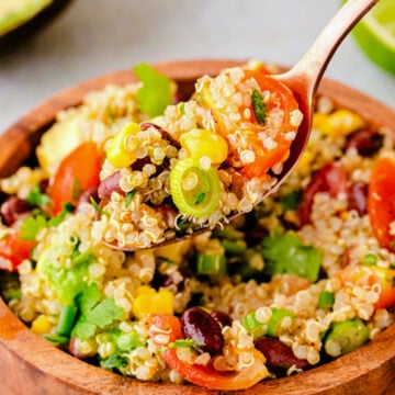 Wooden bowl of colorful mexican quinoa 4 salad with red peppers, corn, beans, cilantro, and green onions on wooden spoon