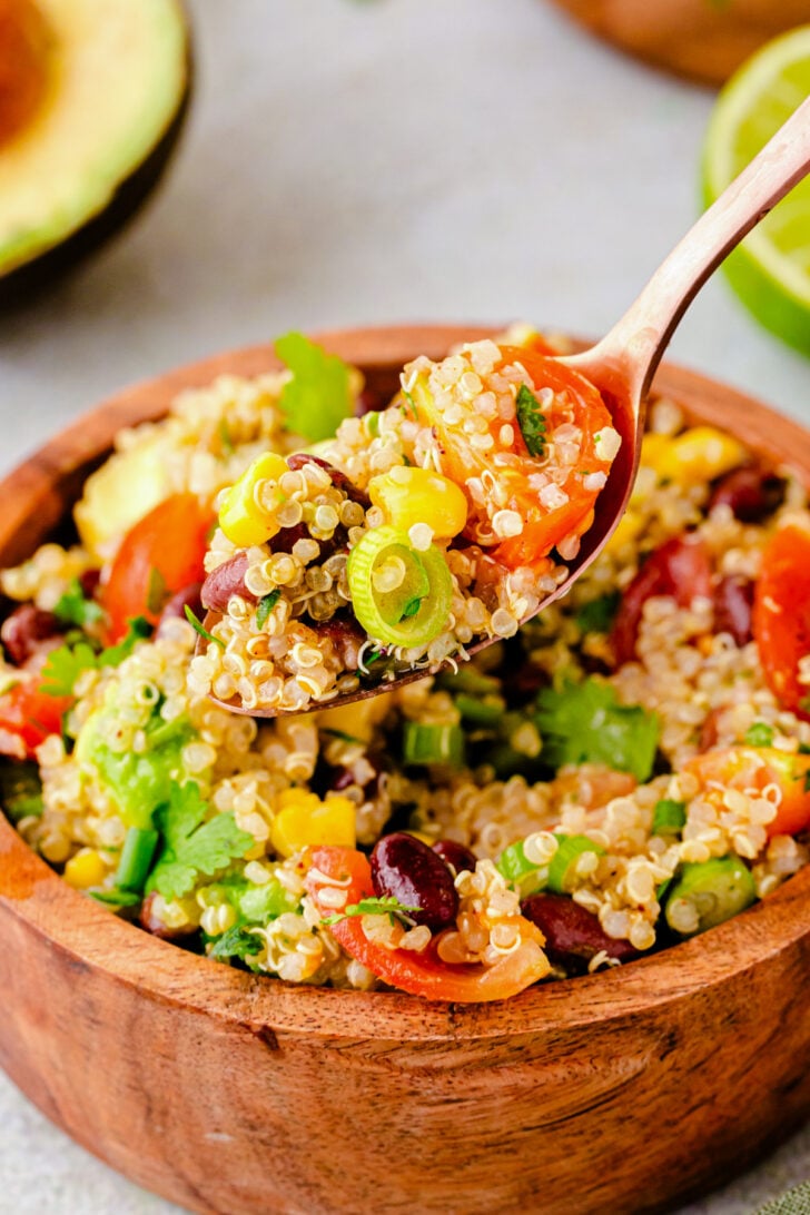 Wooden bowl of colorful mexican quinoa 4 salad with red peppers, corn, beans, cilantro, and green onions on wooden spoon