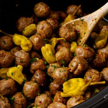 Crock Pot Mississippi Meatballs in a slow cooker with pepperoncini peppers and fresh chives garnish, wooden spoon stirring