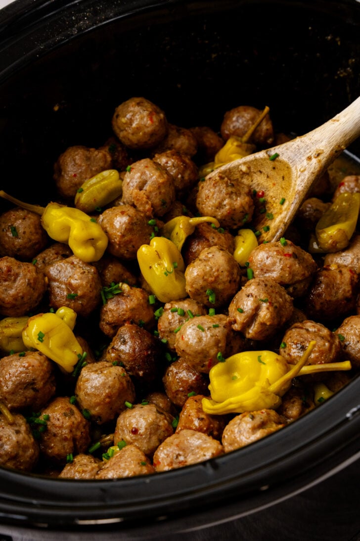 Mississippi meatballs in a crock pot with a wooden spoon mixing.