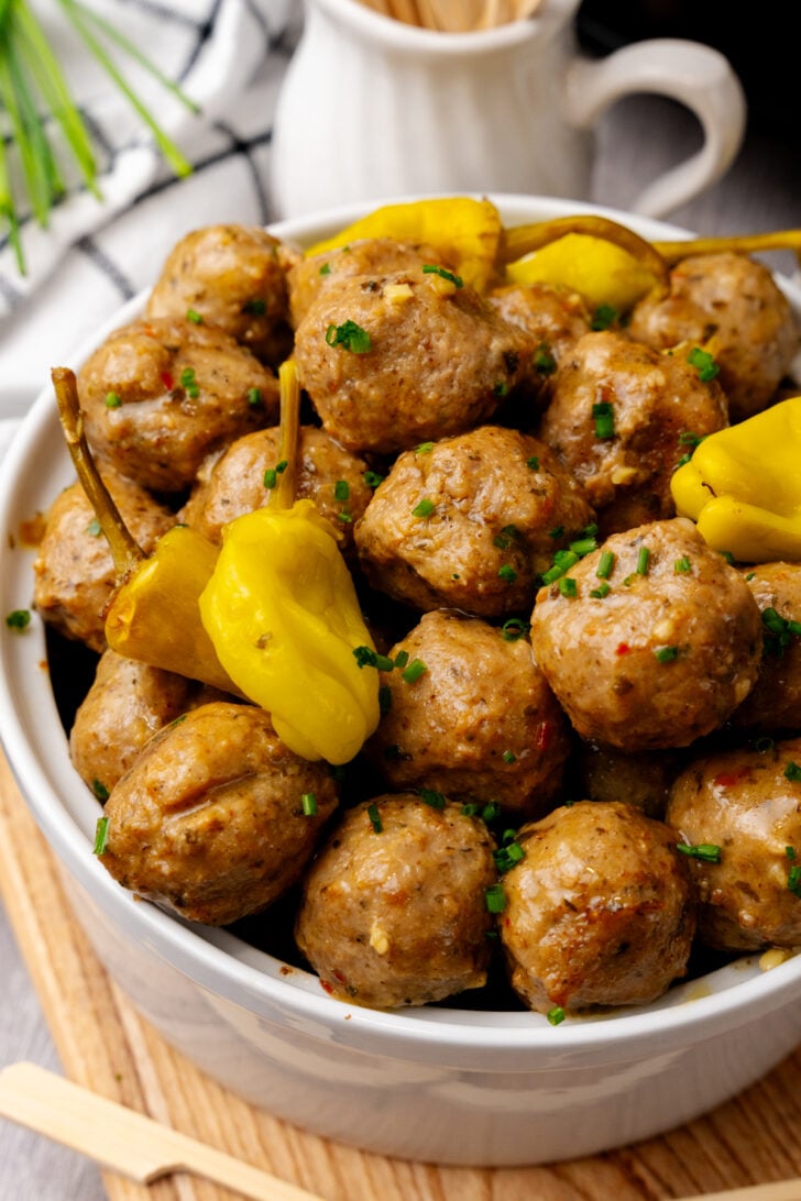 Meatballs in a white bowl with yellow peppers topping it.