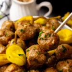Crock Pot Mississippi Meatballs on white plate with yellow peppers, garnished with green onions and served with wooden spoons