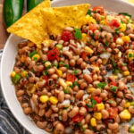 Southern caviar 6 bean dip in white bowl with tortilla chips, corn, peppers, and cilantro garnish, wooden surface