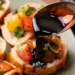 Balsamic reduction drizzled over bruschetta topped with diced tomatoes, peppers, and fresh basil on a gray plate
