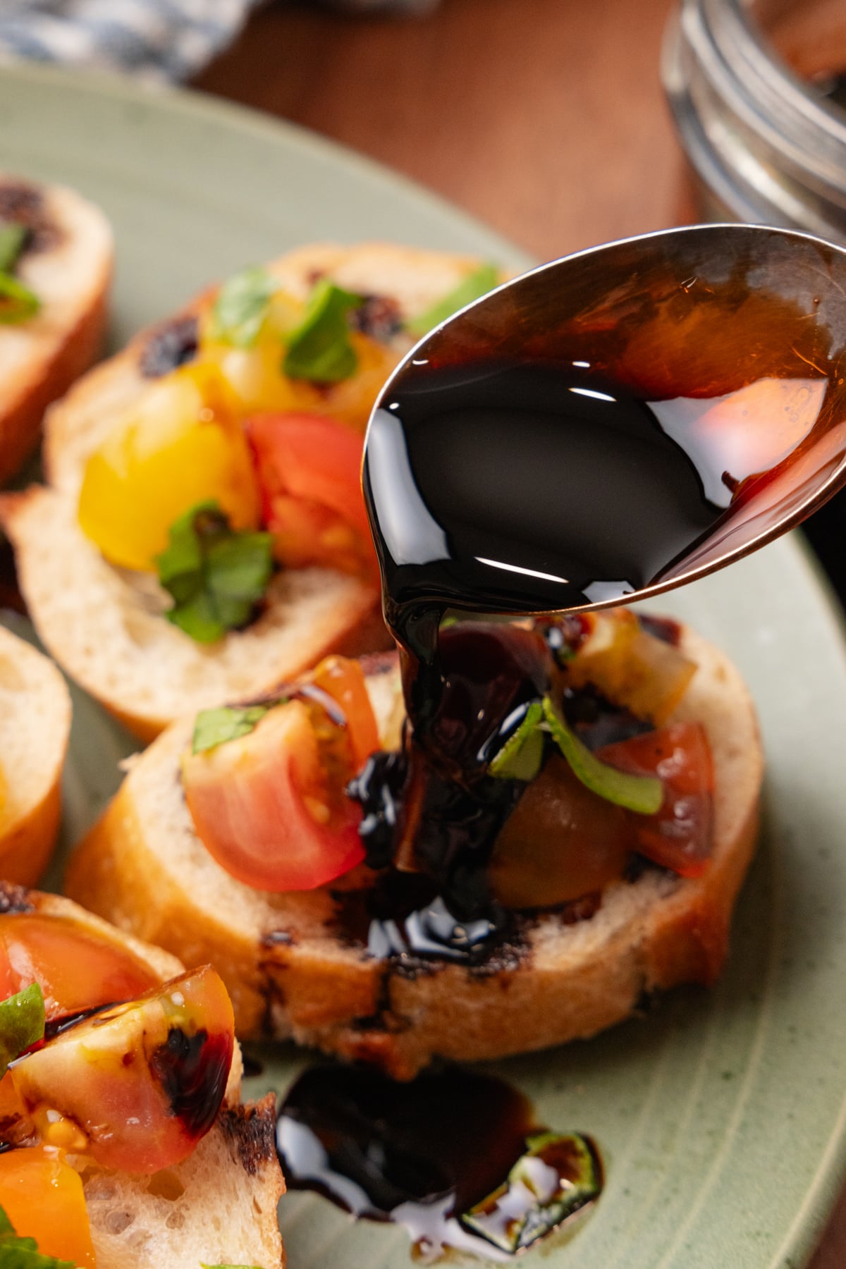 Balsamic reduction drizzled over bruschetta topped with diced tomatoes, peppers, and fresh basil on a gray plate