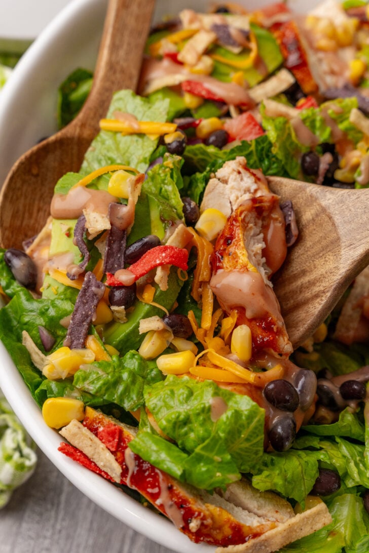 BBQ chicken salad being tossed with wooden salad utensils.