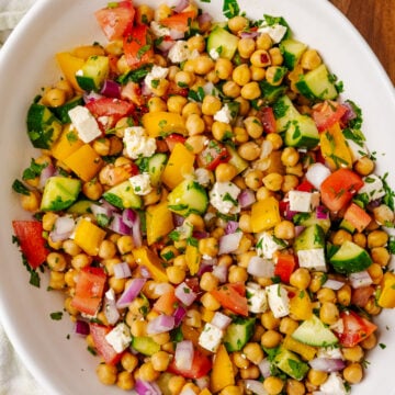 Overhead view of colorful Chickpea Salad on white plate with cucumbers, tomatoes, bell peppers, red onions, feta cheese, and fresh parsley