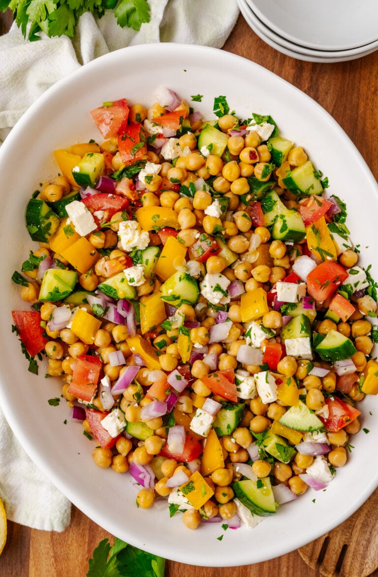 Overhead view of colorful Chickpea Salad on white plate with cucumbers, tomatoes, bell peppers, red onions, feta cheese, and fresh parsley